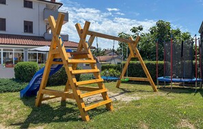 A wooden swing set and slide in a grassy yard with a house in the background.