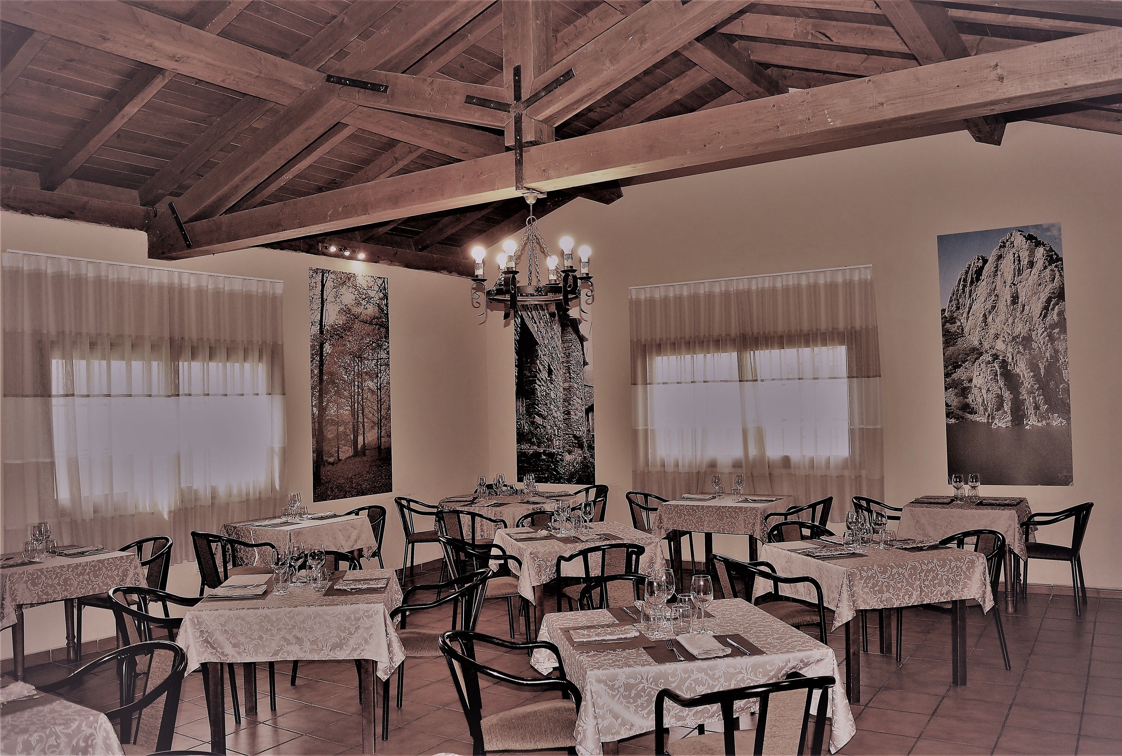 A dining area with tables set for service, wooden beams on the ceiling, and artwork on the walls.