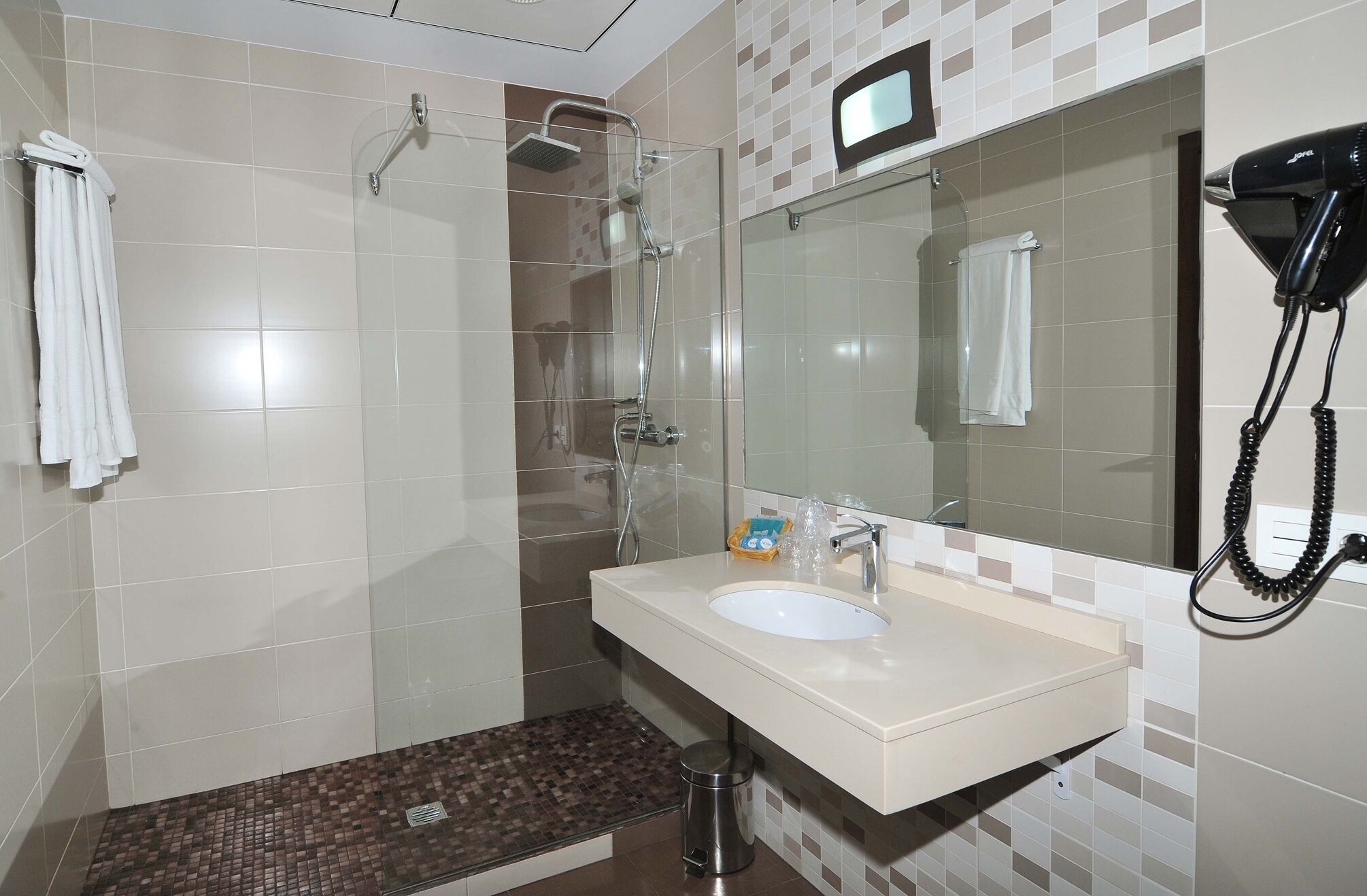 Une salle de bain moderne avec une douche à parois de verre, un lavabo avec un miroir et un sèche-cheveux fixé au mur.