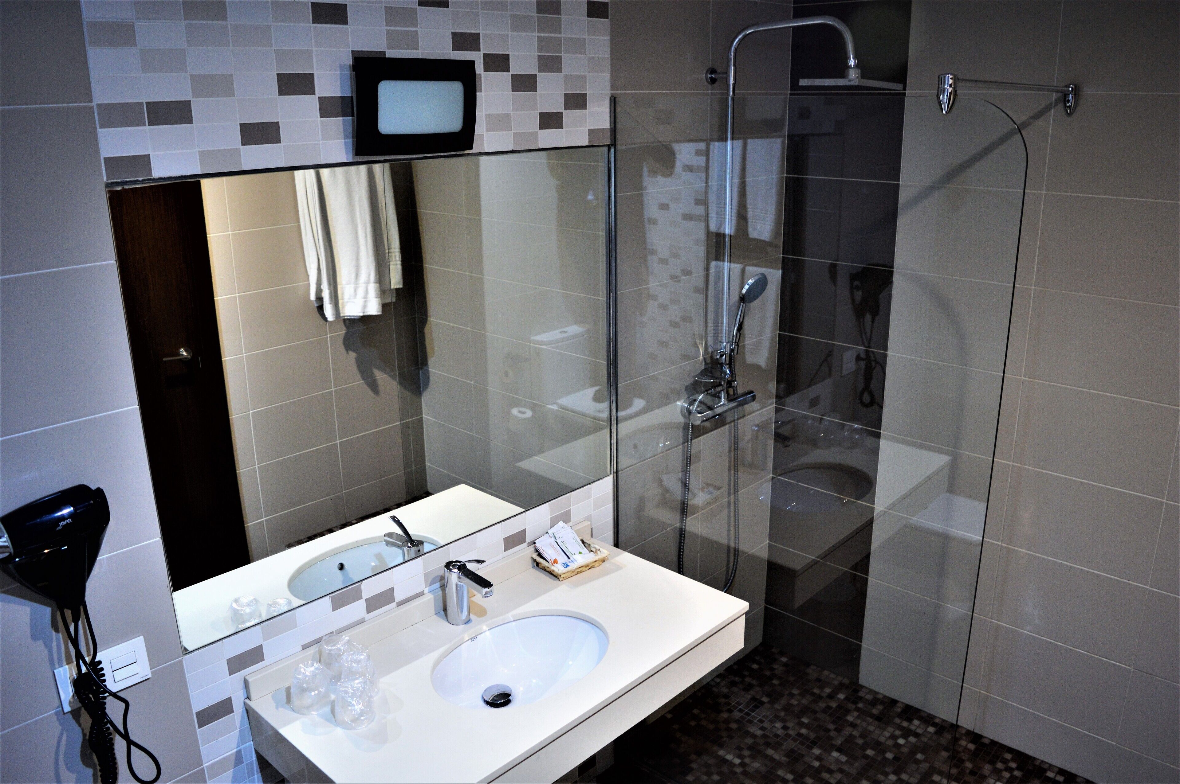 Un bany modern amb plat de dutxa envoltat de vidre, un lavabo blanc i un mirall a sobre.