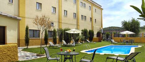 Un patio de hotel con piscina, sillones de descanso y una pequeña mesa con bebidas.