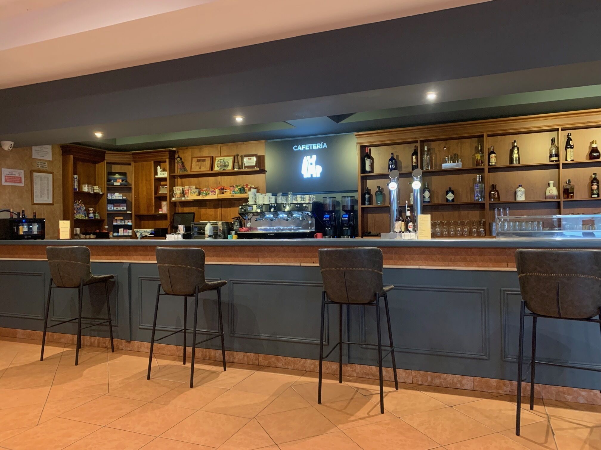 A bar area with a counter, bar stools, and shelves stocked with bottles and glasses.