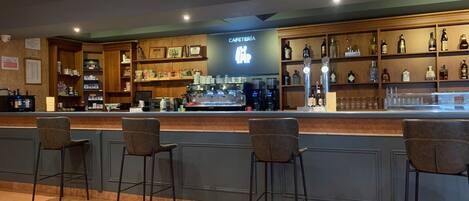 A bar area with a counter, bar stools, and shelves stocked with bottles and glasses.