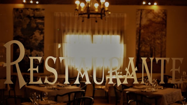 A restaurant interior with tables set for dining, a chandelier, and a large window with curtains. - Hotel Ciudad de Plasencia (Plasencia)