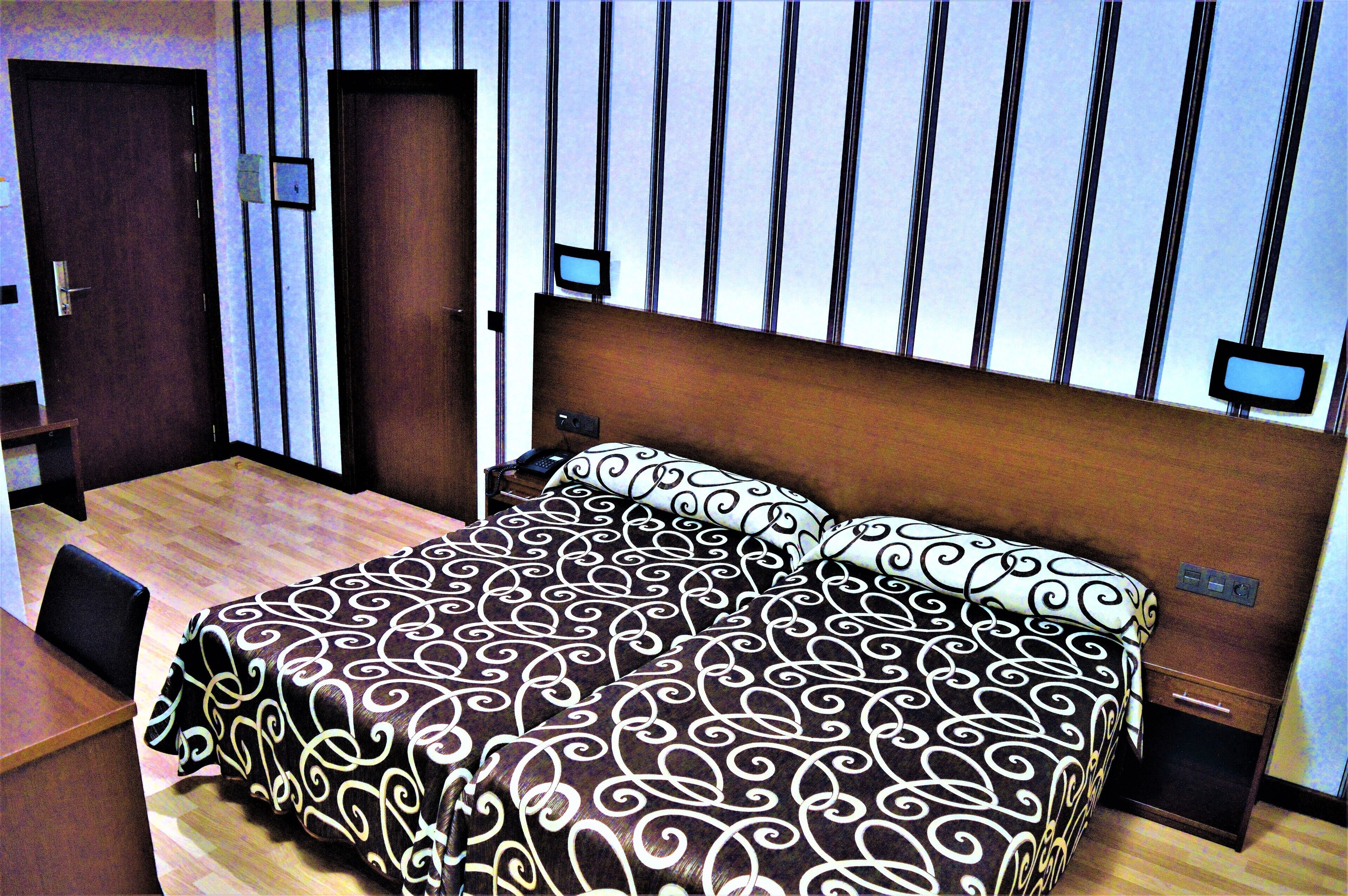 Een hotelkamer met een houten bed, een klein bureau en een televisie aan de muur.