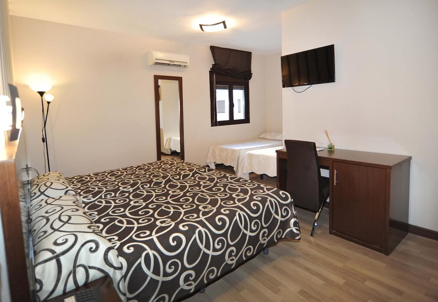 Une chambre à coucher comprenant un lit, un bureau, une chaise, un climatiseur, un miroir et un téléviseur.