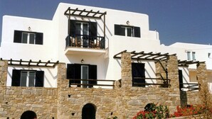 A white building with stone walls, multiple windows, and balconies. - San Antonio Summer House by GHH (Paros)