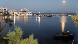A marina with boats docked, a building with multiple floors, and a calm water body reflecting the moon. - San Antonio Summer House by GHH (Paros)