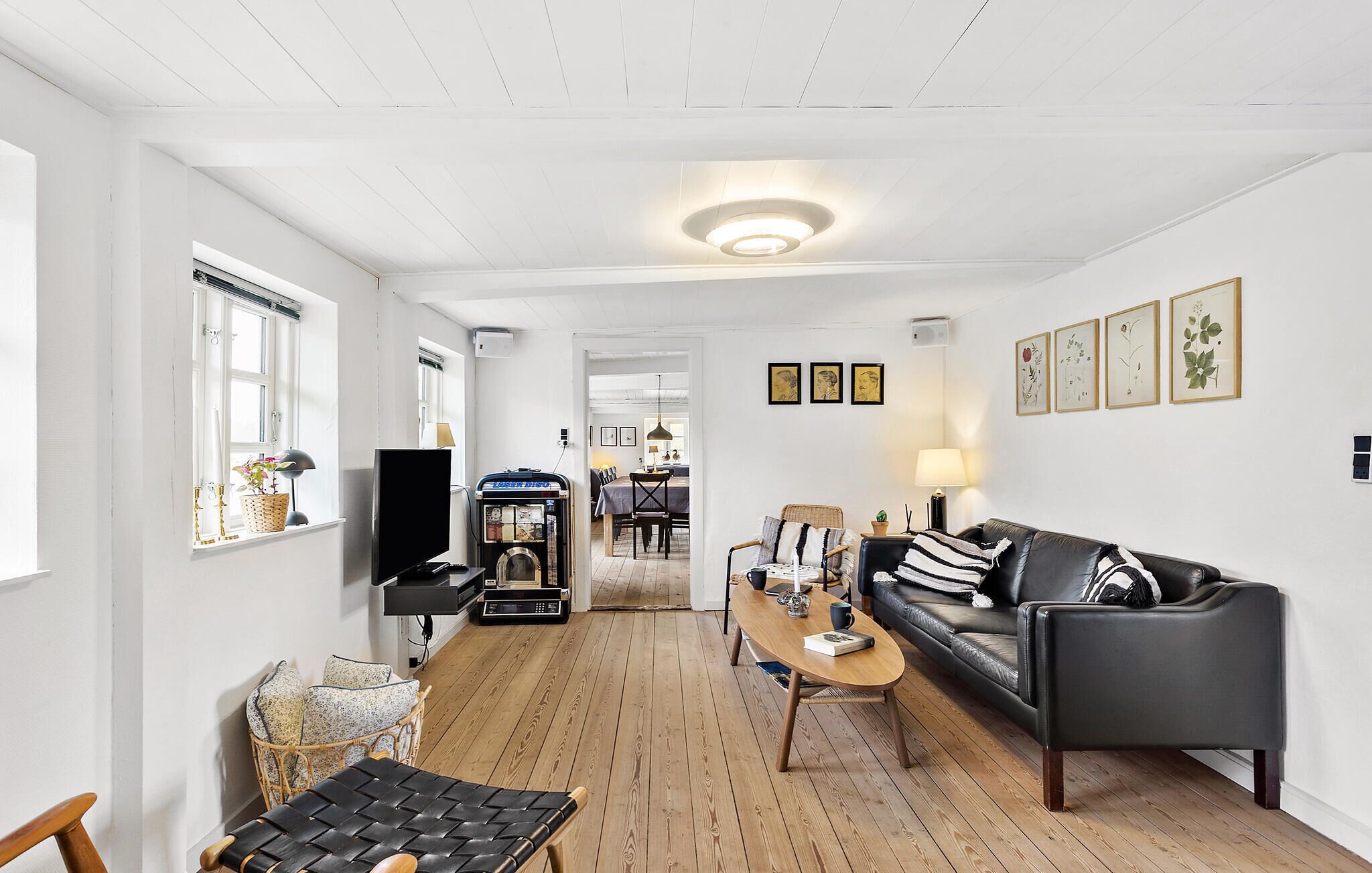 Amplia sala de estar con piso de madera, un sofá de cuero negro, una mesa de comedor y un televisor.