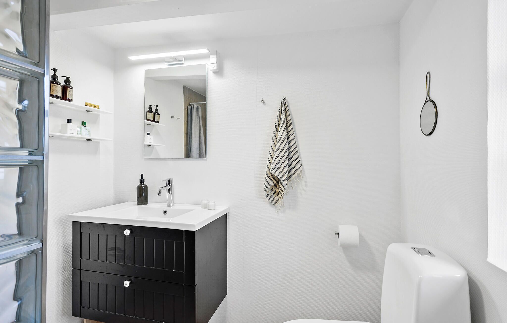 Un baño moderno con un lavabo blanco, muebles negros, un perchero y un dispensador de papel higiénico.
