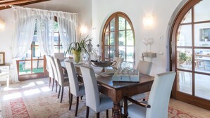 Comedor con mesa de madera, sillas blancas y ventanas arqueadas amplias.