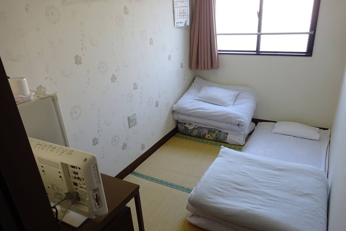 A hotel room with two beds, a desk with a computer, a calendar on the wall, and a window with curtains.