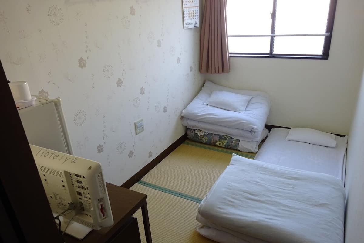 Habitación de hotel con dos camas, un escritorio con computadora, un calendario en la pared y una ventana con cortinas.