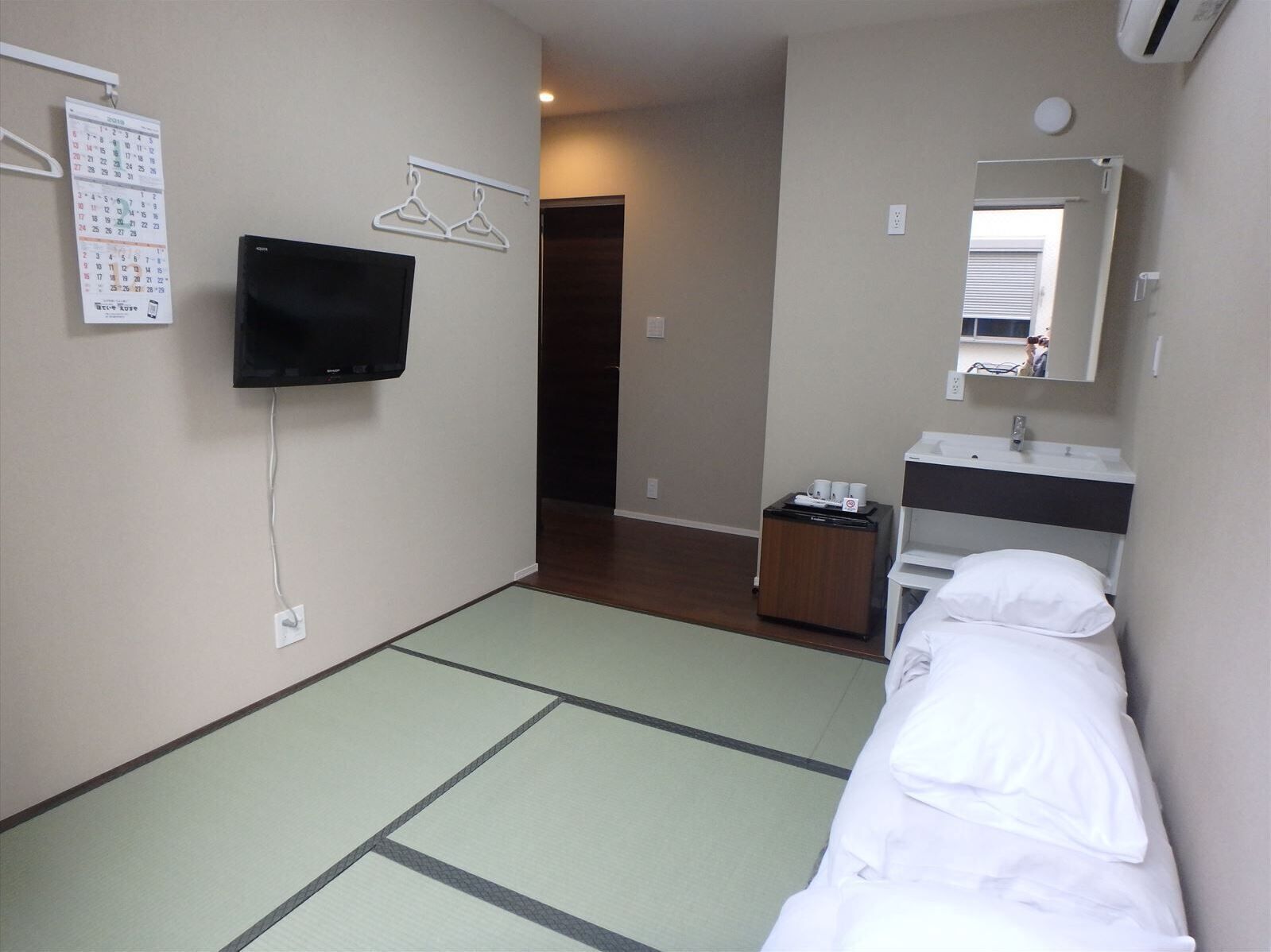 Une chambre d’hôtel avec un lit, un téléviseur fixé au mur, un calendrier et un miroir au-dessus du lavabo.