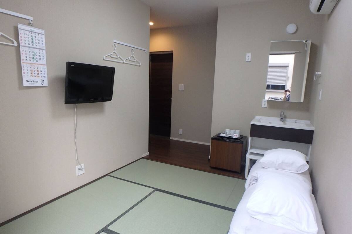 A hotel room with a bed, a TV mounted on the wall, a calendar, and a mirror above the sink.