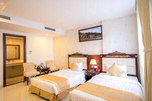 Une chambre d’hôtel avec deux lits, un coin salon avec des fauteuils, une petite table et un tableau au mur.