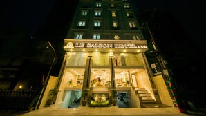 Het exterieur van Hotel Le Saigon 's nachts, met een opvallende ingang met een bord, een trap naar de ingang en een goed verlichte gevel.
