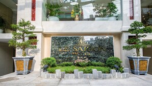 De ingang van Le Saigon Hotel, met een opvallend bord, plantenbakken en een verzorgd tuingedeelte.