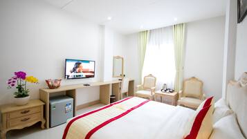 Une chambre d’hôtel équipée d’un lit, d’un bureau, d’une télévision, d’un miroir, d’une chaise, d’une table de chevet et d’un petit réfrigérateur.