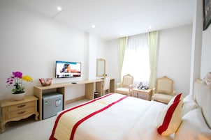 A hotel room with a bed, a desk, a television, a mirror, a chair, a nightstand, and a small refrigerator.