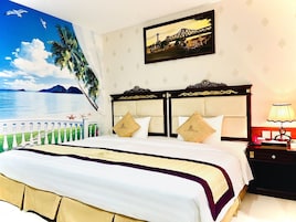 Quarto de hotel com uma cama, uma mesinha de cabeceira, um abajur, um quadro e um mural com uma cena de praia.