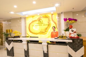 A hotel reception desk with a marble counter, a receptionist, and a floral arrangement.