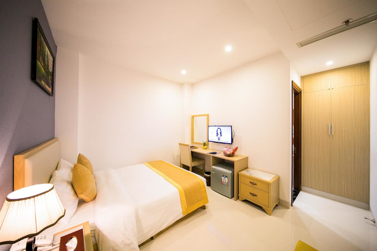 Een hotelkamer met een bed, een bureau met een computer, een kleine koelkast, een nachtkastje en een kledingkast.