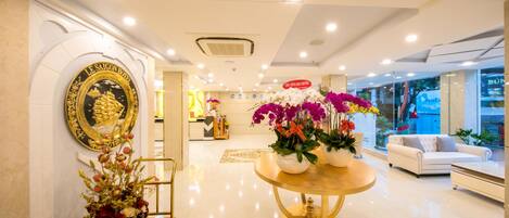 A hotel lobby with a reception desk, a decorative archway, a round table with flowers, and a white sofa.