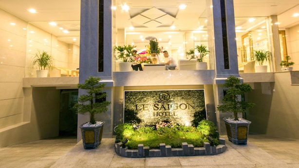 De ingang van Le Saigon Hotel met een goed verlichte gevel, een centrale ingang en potplanten rondom het entreegebied.