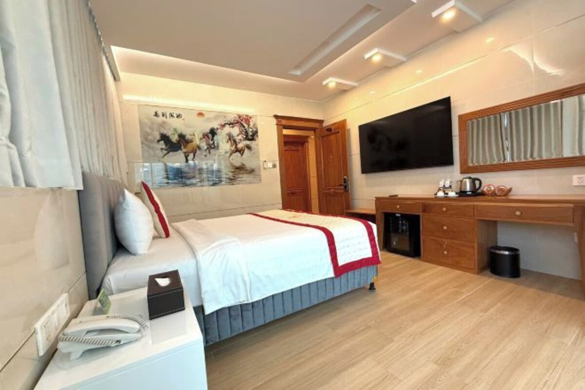 Een moderne hotelkamer met een bed, nachtkastje, televisie en een bureau met een stoel.