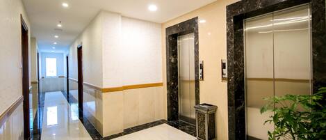 A modern hotel corridor with marble flooring, two elevators, and a potted plant.