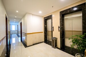 A modern hotel corridor with marble flooring, two elevators, and a potted plant.