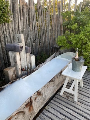 A wooden bench with a white table beside it, a bottle of champagne, and a glass on the table.