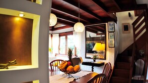 Un comedor con una mesa de madera, sillas, una cesta de frutas e lámparas colgantes.