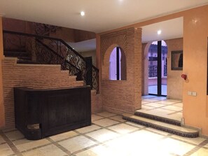 En trappe med dekorativt metalgelænder, et receptionsområde og udsigt til en balkon.