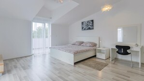 Una moderna camera da letto con un letto, comodini, una scrivania, una sedia, un'ampia finestra e una lampada a sospensione.