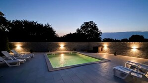 Una piscina esterna rettangolare circondata da un muro in pietra, dotata di illuminazione.