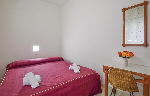 A hotel room with a single bed, a desk, a chair, and a mirror.