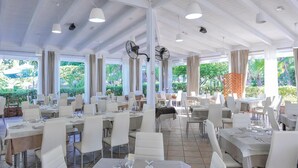 Un restaurant spacieux avec de hauts plafonds, de grandes fenêtres et des meubles blancs.