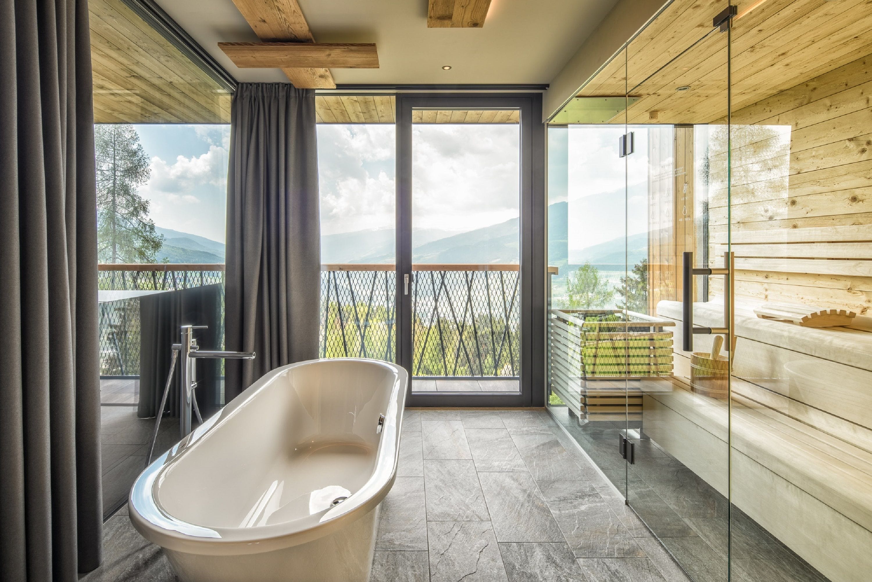 Un baño moderno con una bañera independiente, ventanas amplias y vistas a montañas.