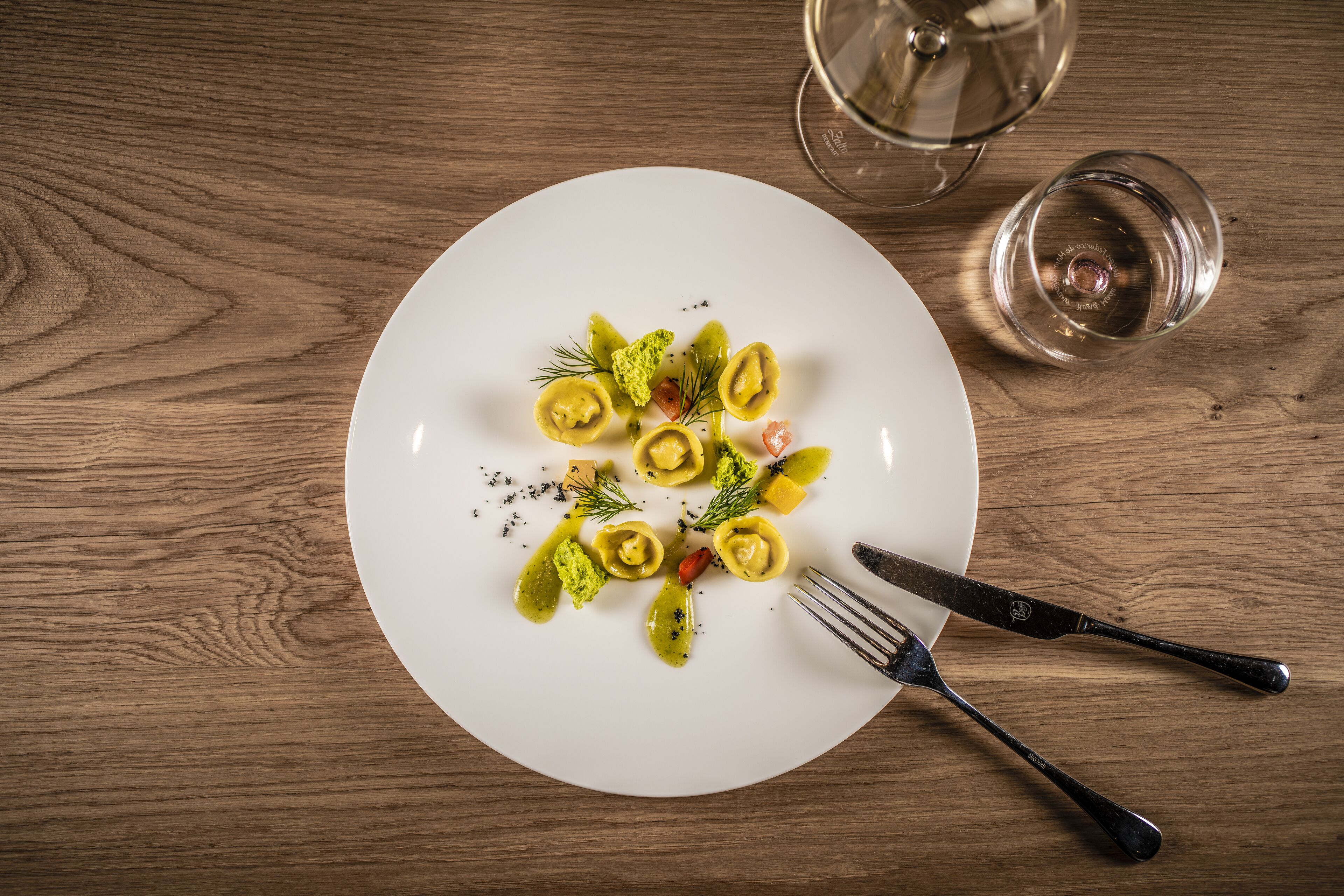 Un piatto bianco con ravioli, guarniti con erbe aromatiche e salsa, su un tavolo di legno.
