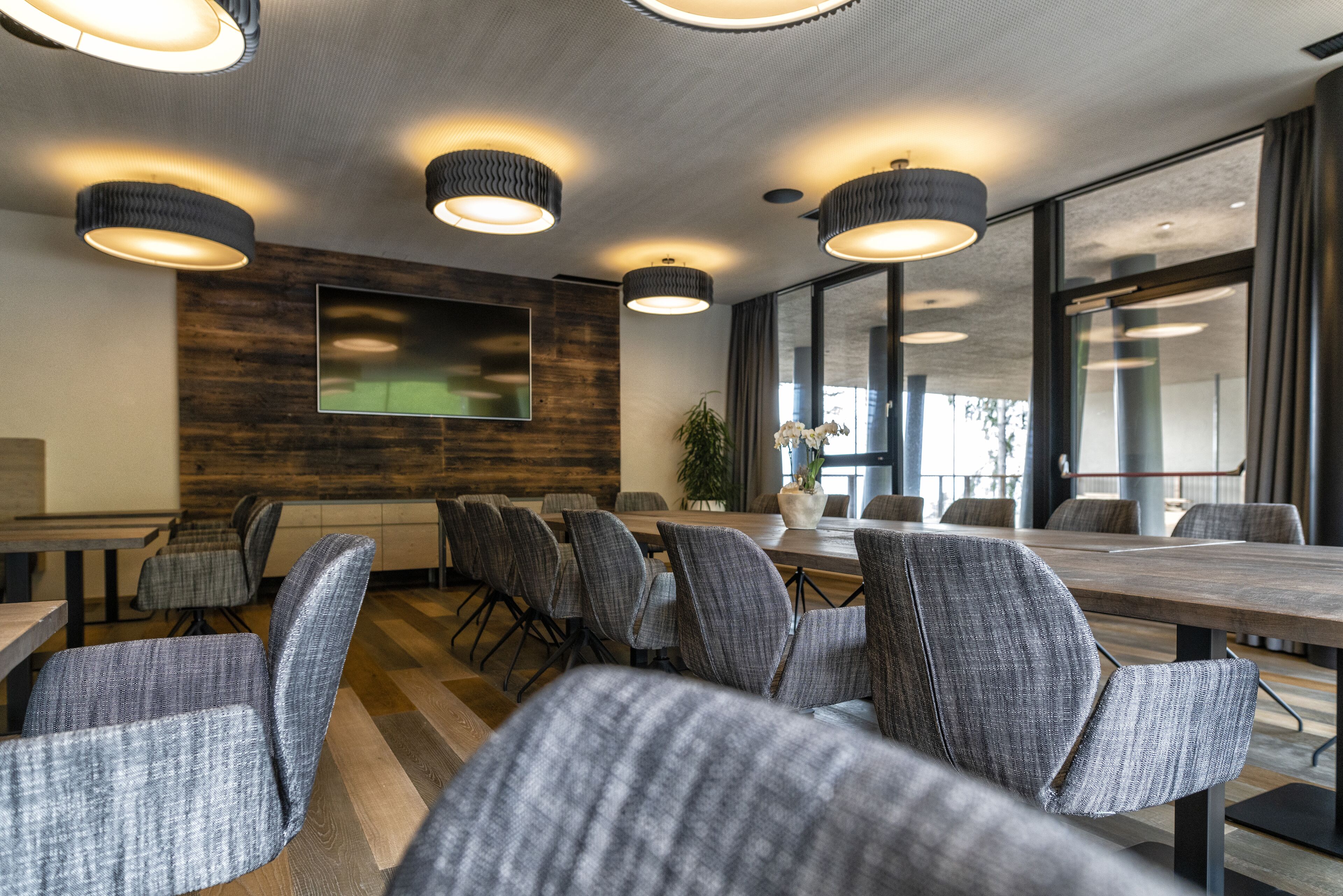 A conference room with grey upholstered chairs, a wooden table, and pendant lighting.