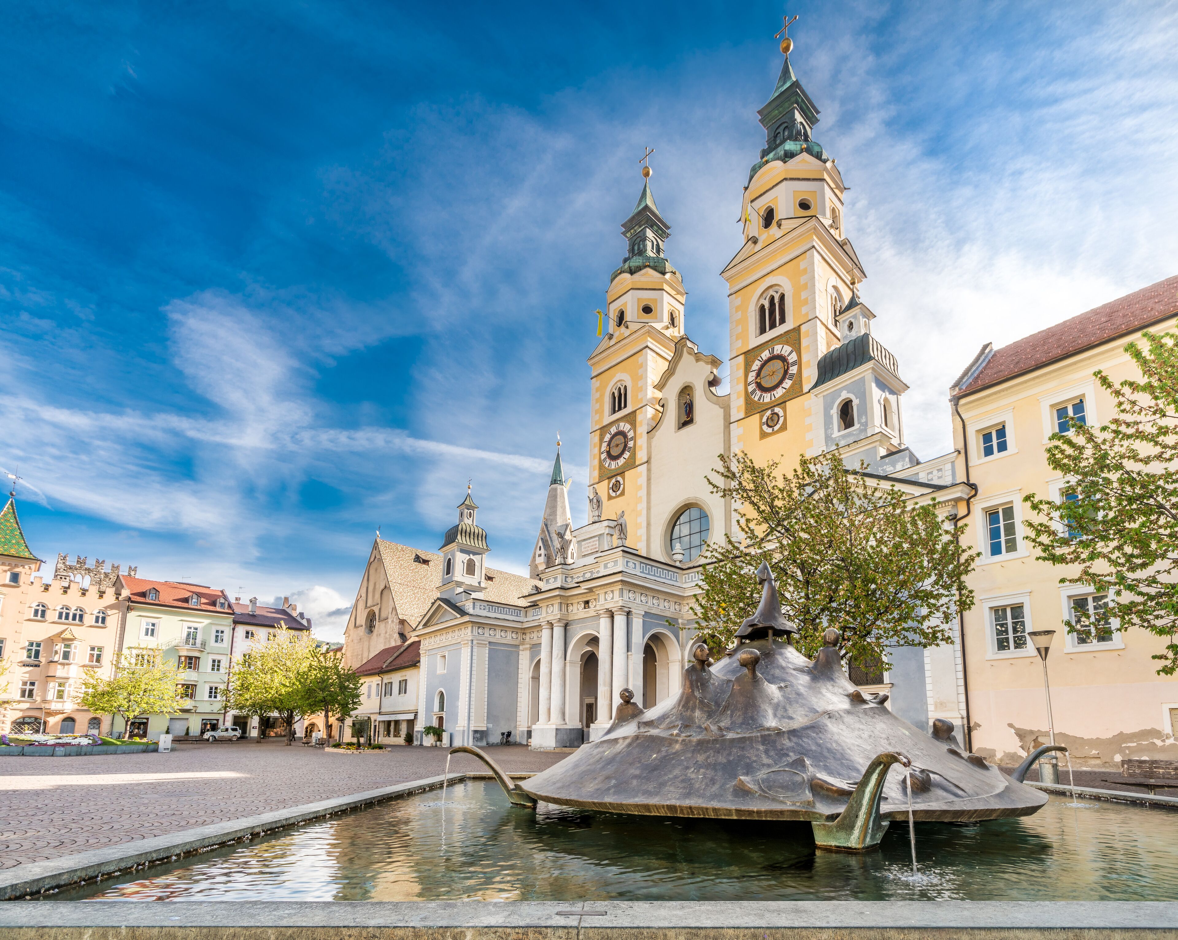 A historic church with two towers and a central dome, surrounded by a cobblestone square and a fountain.