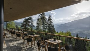 Une terrasse extérieure, agrémentée de tables et de chaises, qui offre une vue sur un paysage montagneux.