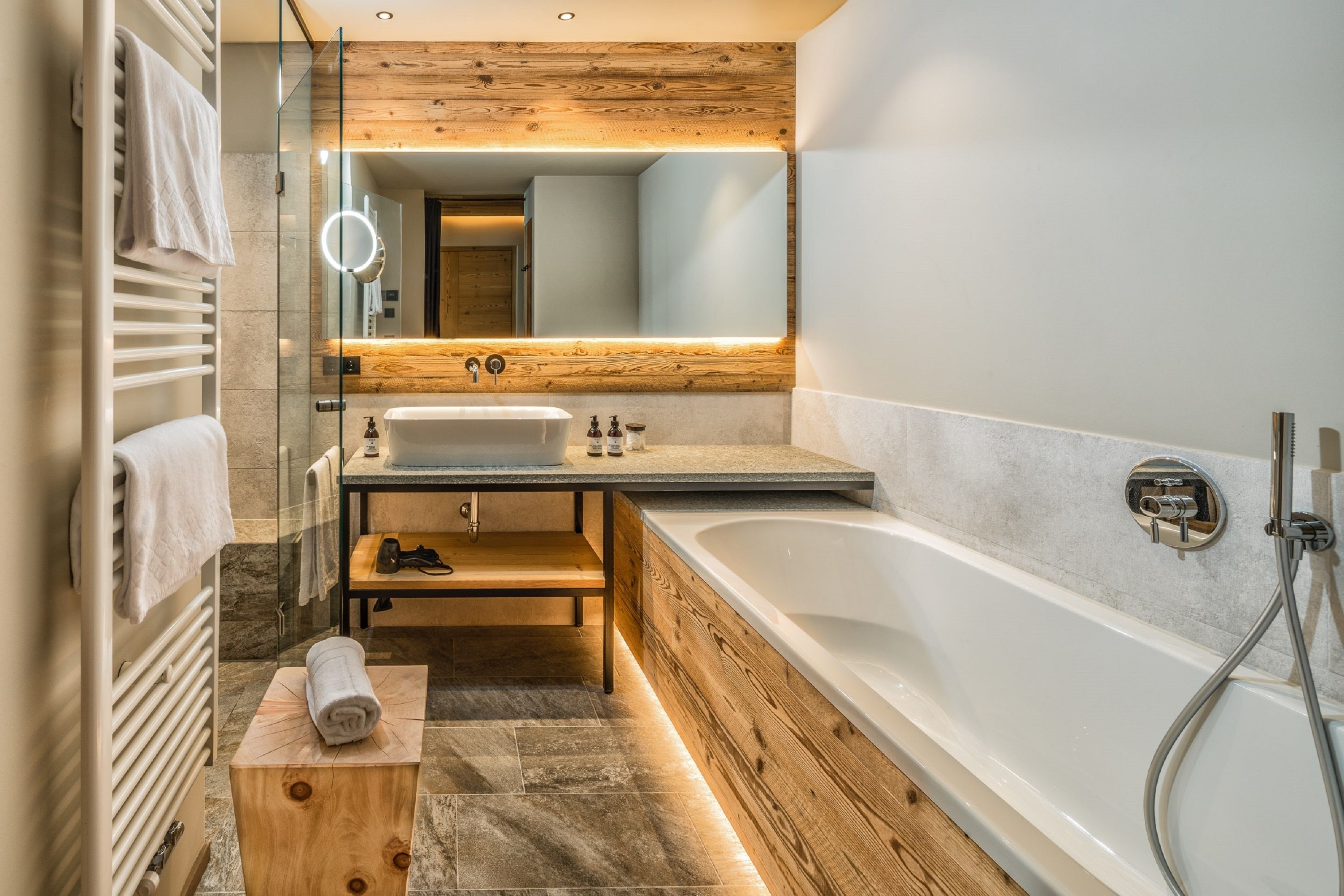 Une salle de bain moderne avec un meuble-lavabo en bois, une grande baignoire et une douche séparée par une paroi de verre.