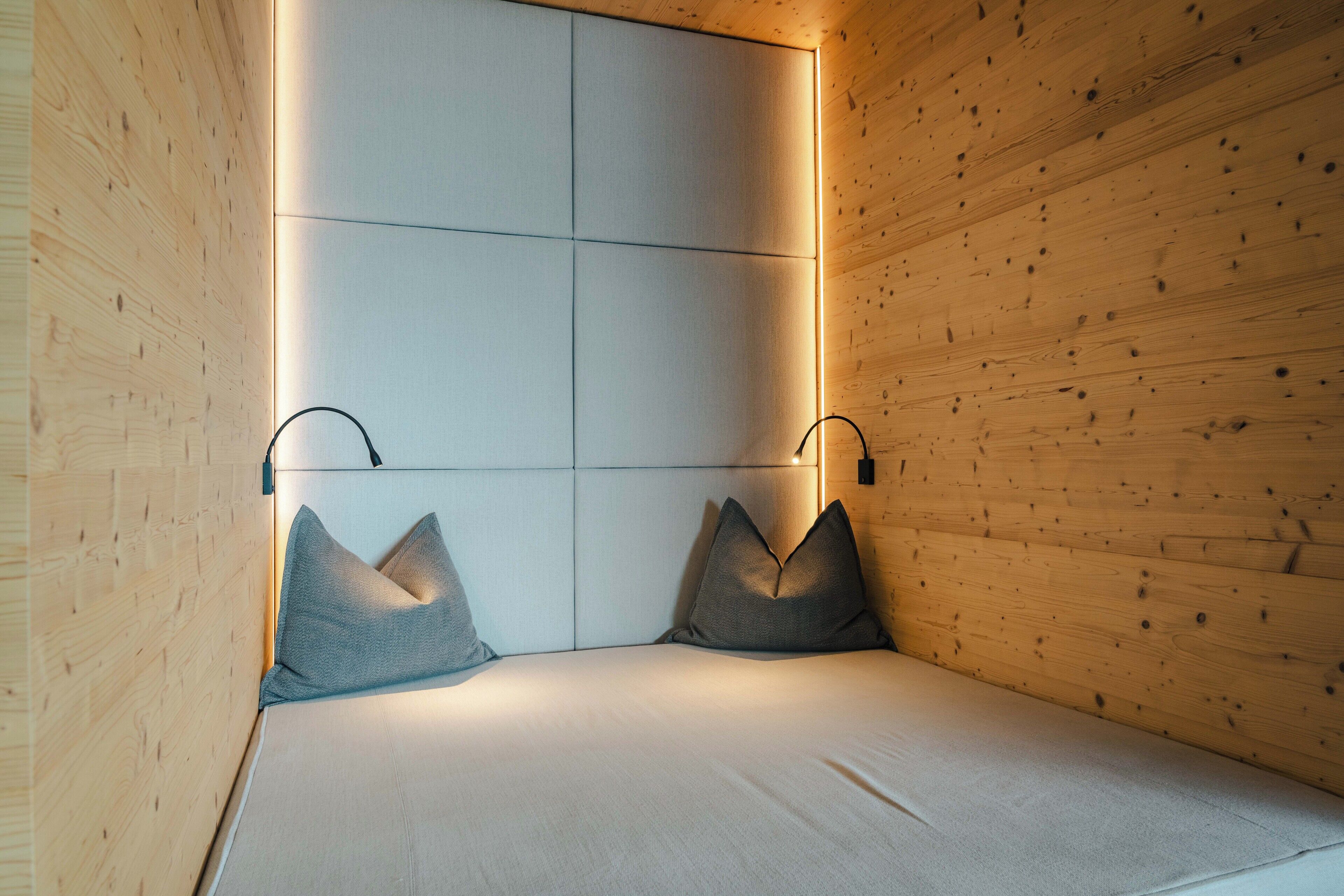A modern room with wooden panel walls, a bed with grey bedding, and two wall-mounted light fixtures.