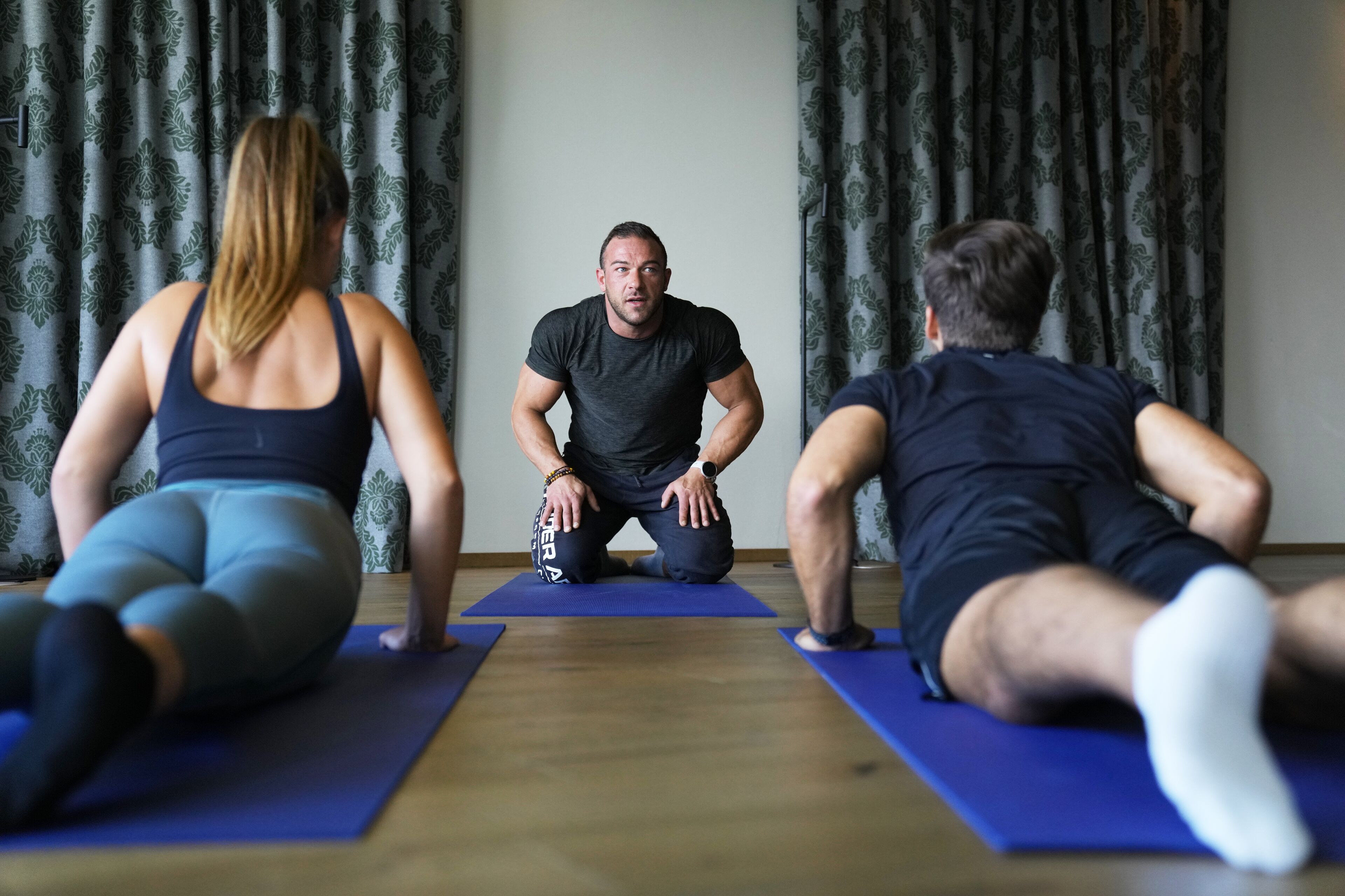 Trois personnes sur des tapis de gymnastique dans une pièce décorée de rideaux à motifs.