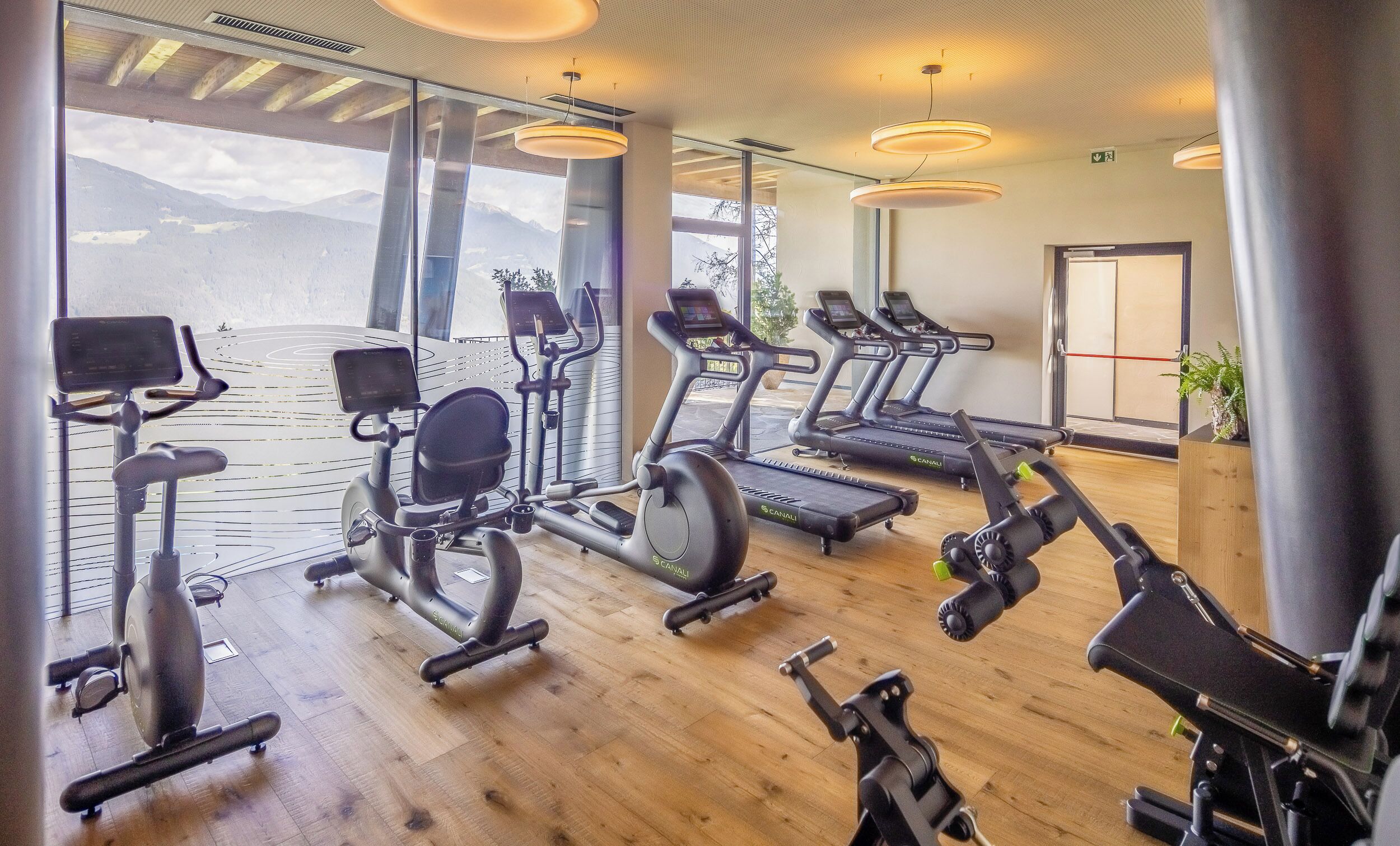 A gym with various exercise equipment, large windows, and a view of mountains.