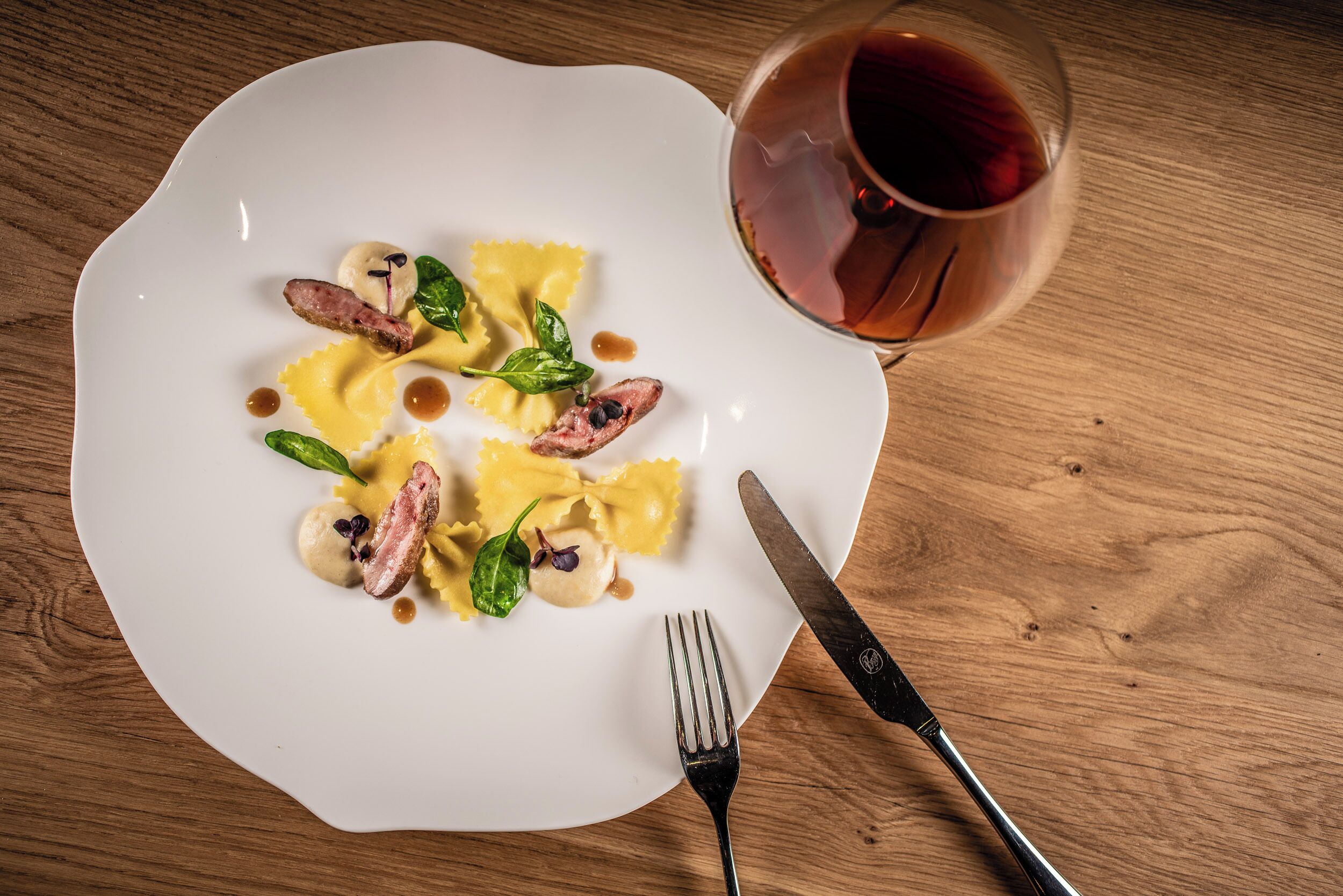 Een witte bord met ravioli, een glas rode wijn en een vork op een houten tafel.