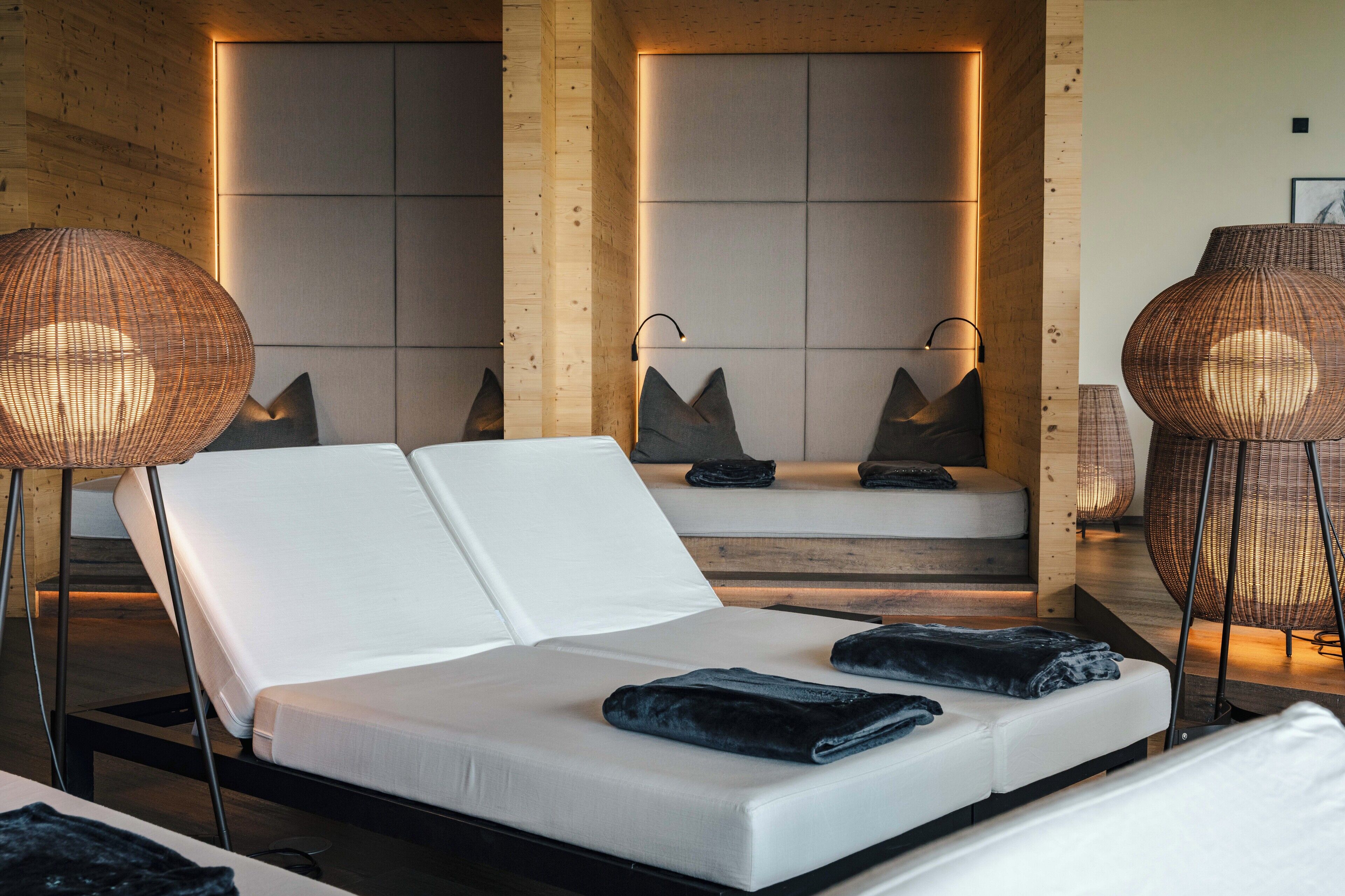 A modern hotel room with a white sofa bed, two large woven floor lamps, and a neutral-toned headboard.